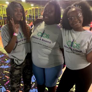 Three students smile together at the arcade during a skating rink field trip with Above and Beyond Students' free summer camp in Charlotte, NC.