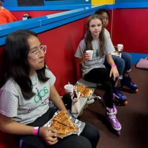 Students and a teacher in roller skates enjoy pizza during a skating rink field trip with Above and Beyond Students' free summer camp in Charlotte, NC.
