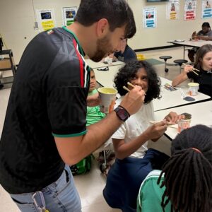 A camp counselor helps a student learn to use chopsticks during Above and Beyond Students' free summer camp cultural activity in Charlotte, NC.