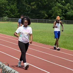Students race down the outdoor track while balancing an item in spoons during an Olympics day game at Above and Beyond Students' free summer camp Olympics, Ranson Middle School, Charlotte, NC.