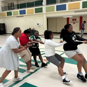 Students play tug of war as a staff member cheers them on in the gym during Above and Beyond Students' free summer camp Olympics at Ranson Middle School in Charlotte, NC.